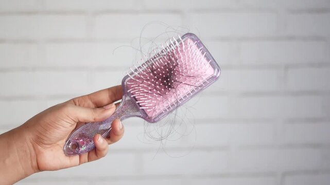 A person holding a hairbrush full of tangled hair, showcasing hair loss problem in close-up motion shot