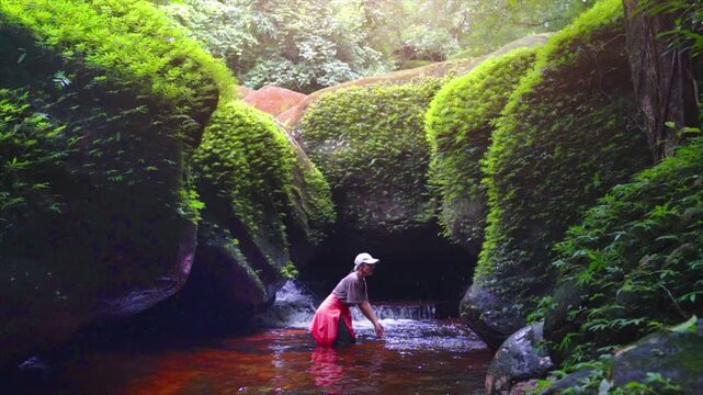 An Asian woman splashes water onto a dolphin-shaped rock at Phu Langka National Park, Bueng Kan Province, Thailand.