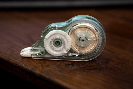 correction tape dispenser with a clear green housing resting on a dark wooden table surface