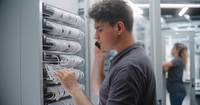 Male Network Engineer Performs Physical Port Audit While Speaking on Smartphone, Checking Rack Connections and Cable Identification During Digital Verification of Data Center Infrastructure.