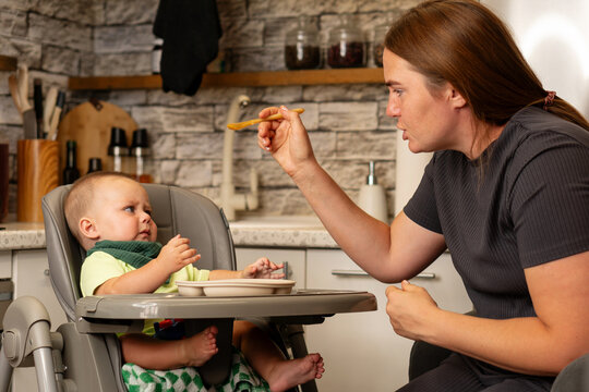 Mother Offers Spoon To Hesitant Baby During Mealtime