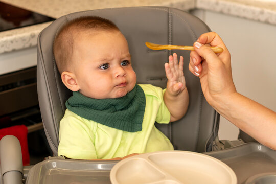 Baby Boy Frowns And Reaches Toward Feeding Spoon