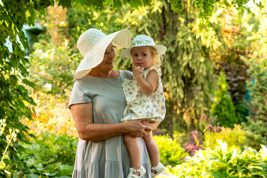 Smiling Grandmother Holding Granddaughter In Sunny Green Garden