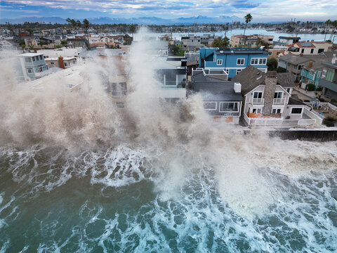 Large waves crash against oceanfront homes during heavy surf, sending spray above seawalls and highlighting the risks of coastal flooding and erosion
