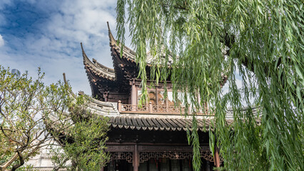 Chinese architecture. A pagoda with curved tiled roofs, ornaments along the edges of the cornices, lattice railings on the terraces. Blue sky, clouds. In the foreground, green willow branches. China   © Вера 