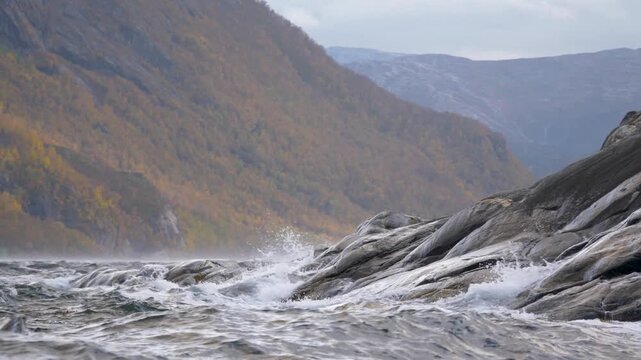 Strong river current flowing over rocks against mountain backdrop in Norway.