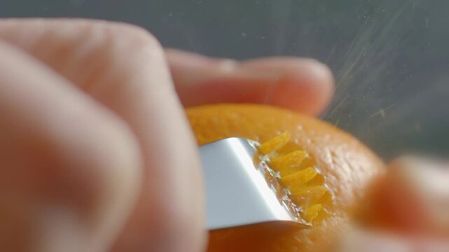 Macro close up of professional chef using zest tool to remove orange citrus peel for garnishing and aromatic ingredient preparation.