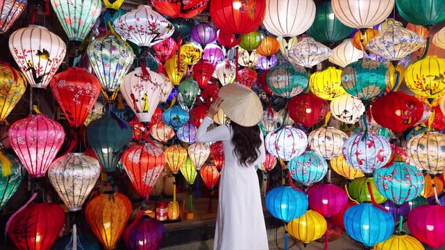 Asian woman wearing Ao Dai Vietnamese dress with colorful lanterns, traveler sightseeing at Hoi An ancient town in central Vietnam.