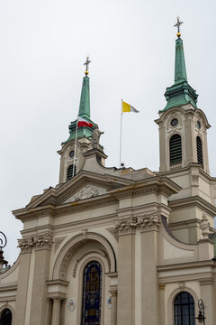 Vertical photo of a catholic church in Poland with a Polish and a Vatican city flags hanging from poles waving in the sky.