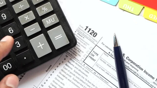 Close-up of hand using calculator on tax form 1120 for corporation income