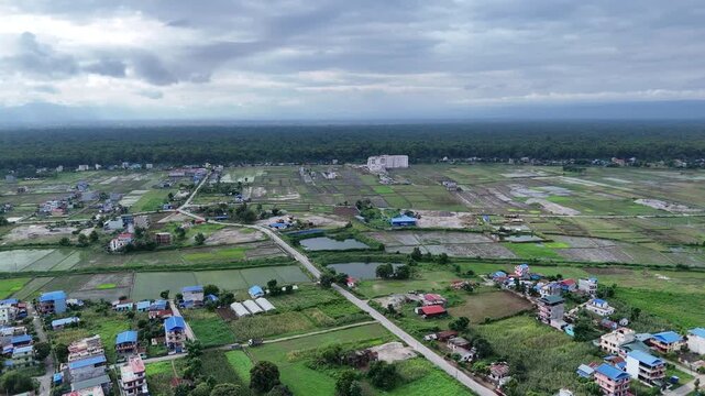 Aerial landscape of a developing rural-urban fringe featuring a crossroads, mixed agricultural plots, scattered housing, and a prominent white commercial building