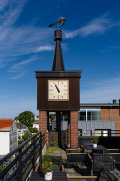Modern clock tower on rooftop terrace with outdoor furniture under blue sky