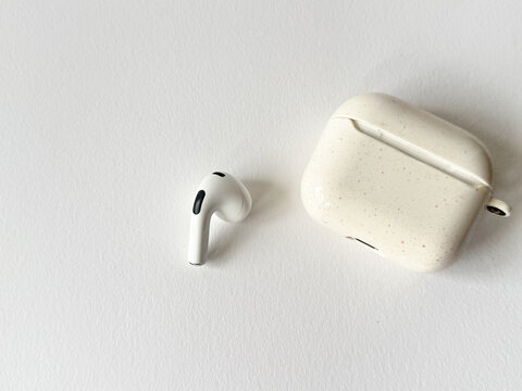 A white earbud next to a closed charging case against a white background
