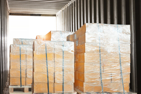 Bulk of Package Boxes Loaded into Shipping Container. CardBoard Boxes Wrapped Plastic on Pallets. Supplies, Supply Chain, Shipment Goods. Distribution Warehouse Logistics. Freight Transportation.	
