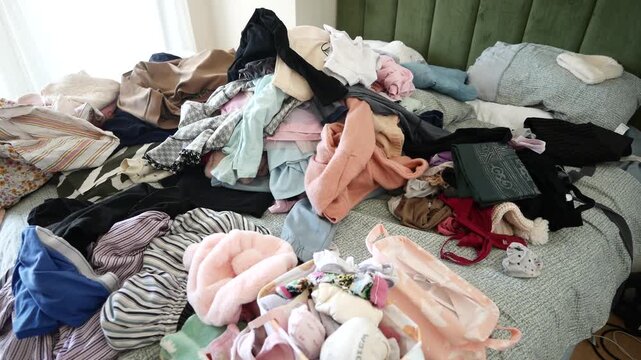 Messy pile of colorful clothes scattered on bed in brightly lit bedroom