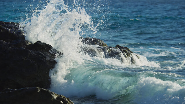 Ocean waves crashing against dark volcanic rocks with white foam