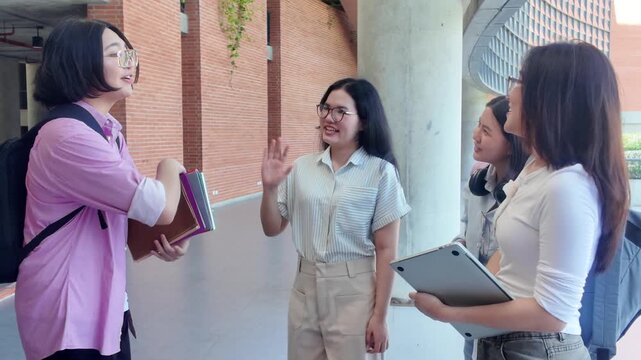 Group of smiling young university students handing over books and greeting each other on campus, happy college friends sharing study materials and waving goodbye in university hallway