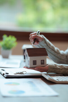 Real estate professional holding a model house at a desk with property documents, representing home ownership, mortgage, investment, and property transactions.