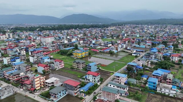 Aerial drone view of a sprawling suburban town with colorful houses expanding into green agricultural fields in Nepal