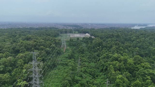 Expansive aerial landscape showing a vast dense green forest interrupted by a high voltage utility corridor and a distant landfill site