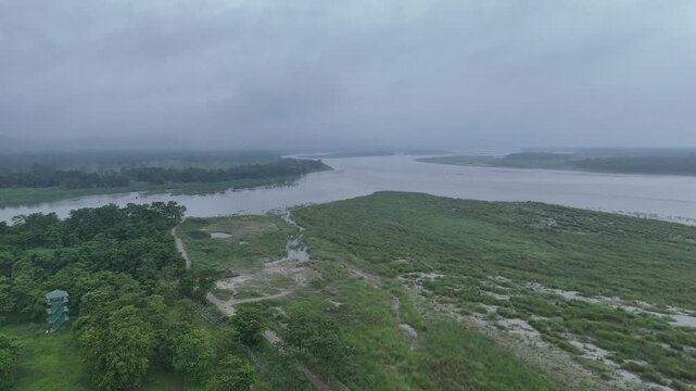 Aerial landscape of a massive muddy river confluence meeting vast green floodplains under a gloomy overcast sky in Nepal