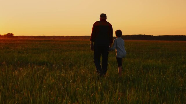 Grandfather and child walking hand in hand through peaceful countryside field at golden sunset, sharing quiet moments of connection, love, and intergenerational bond