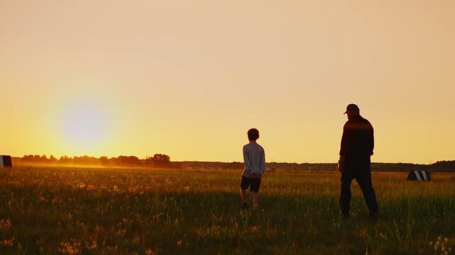 Silhouettes of an elderly man and child walking through a peaceful meadow at golden sunset, sharing a quiet intergenerational moment in the glowing evening light