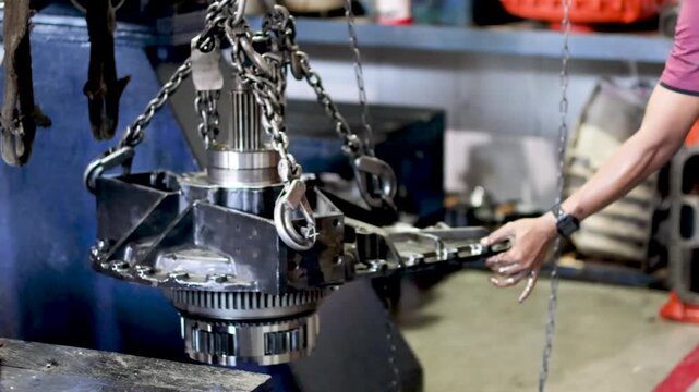 Mechanic positioning a heavy planetary carrier with chain hoist in industrial workshop.