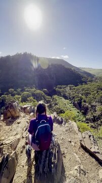 A girl sits on the edge of a ridge, overlooking the meandering river below, along the Werribee Gorge Circuit Walk, near Melbourne, Victoria, Australia.