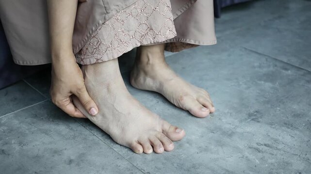 Close up motion footage of young woman suffering from leg pain while sitting on the floor indoors