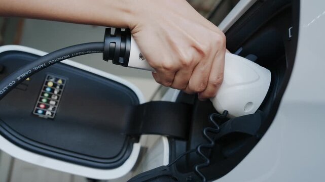 Person plugging in EV charging cable to white electric vehicle for sustainable energy transport.	