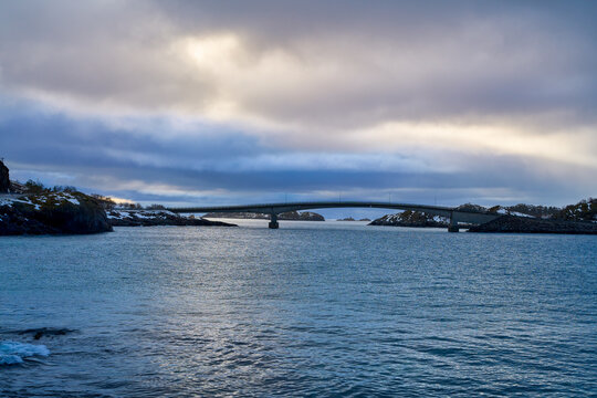 Modern concrete bridge connecting islands over the sea fjord in Lofoten, Northern Norway. Scenic Arctic landscape during a winter road trip adventure. Dramatic cloudy sky over Scandinavian coastal inf