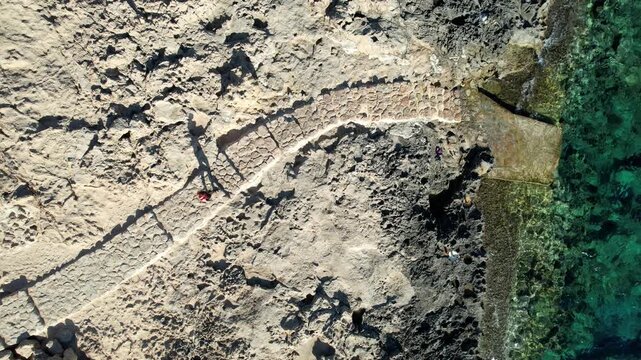 Drone aerial 4k ultra high definition footage of lone person walking along a curved stone pathway on a rocky coastline clear turquoise water. Cape Greko peninsula Cyprus
