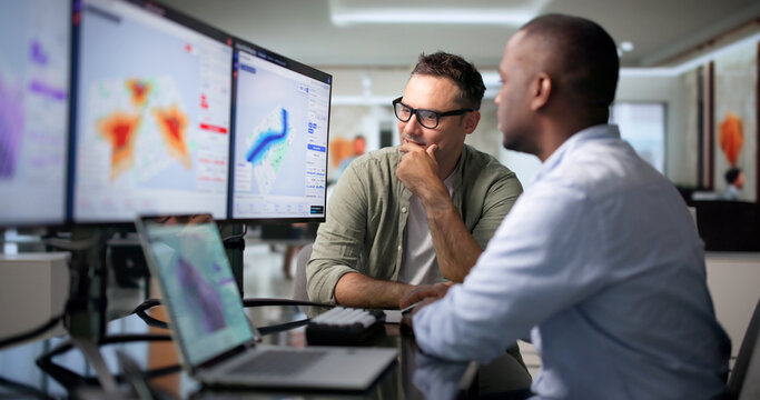Geospatial Analyst And Colleague Reviewing Flood Risk Maps