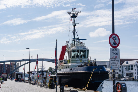 August 19, 2026, Haugesund, Norway - Tugboat VB FLOR&Oslash; docked at a pier with Norwegian flags, a bridge, and buildings in the background.