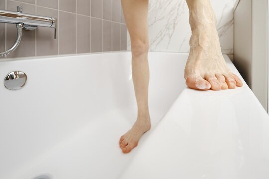A person balances on the edge of a bathtub, showcasing a moment of daily life. The bathroom features light tiles and a sleek design, emphasizing the simplicity of the setting