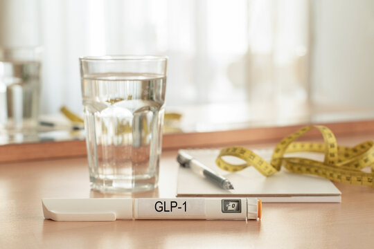 GLP-1 injection pen, measuring tape, notebook, and glass of water on wooden nightstand. Concept of medical weight loss, body weight control, health tracking, hydration, and healthy lifestyle