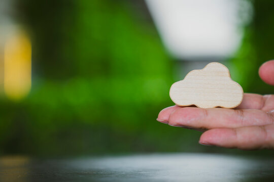 Cloud computing and sustainable IT concept with hand holding wooden symbol against lush green nature bokeh background for digital storage, eco data infrastructure and weather forecast.