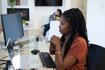 Obraz premium African American women working at glass desk in living room, using laptop and tablet, copy space