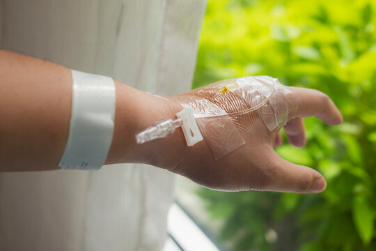 Intravenous therapy and hospital healthcare concept with close up of patient hand with taped iv catheter tube and identification wristband for medical infusion, medicine and clinical care.