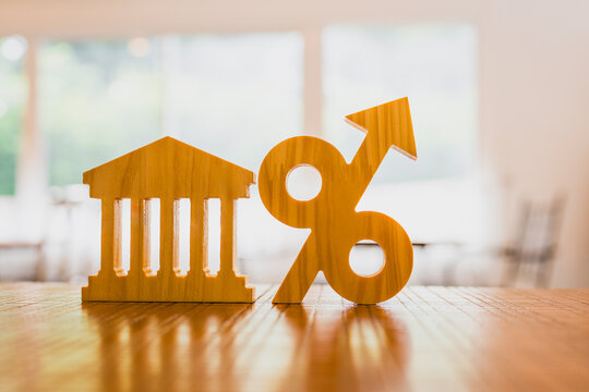 Bank interest rate hike and monetary policy concept with wooden financial building model and upward percent arrow on table for rising borrowing cost, mortgage loan expense and savings yield.