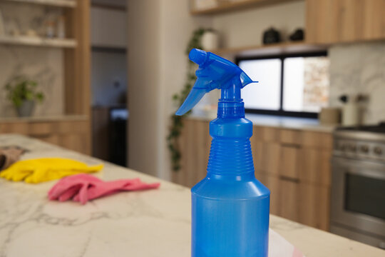 Blue plastic spray bottle sitting on marble countertop with yellow and pink gloves near wide window