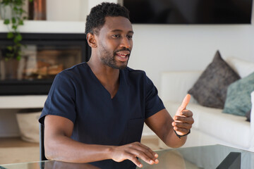 Obraz premium African American man in navy scrubs speaking and gesturing while sitting at glass table at home