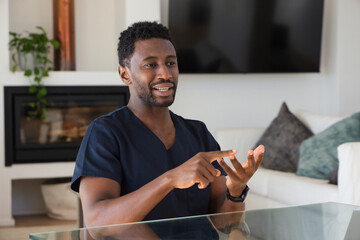 Obraz premium Man in navy scrubs and wristwatch sitting at glass table in living room near TV gesturing