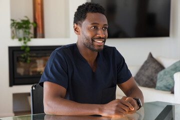 Obraz premium African man sitting at glass table in living room wearing navy scrub top, smartwatch, facing right
