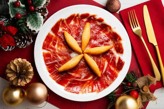 Top view of a spanish tapa Festive premium Iberian ham platter with grissini and Christmas decorations