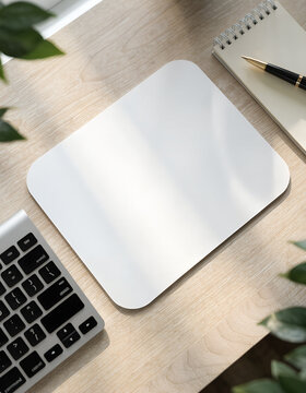 Blank white rectangular mouse pad on a light wood desk with a keyboard, spiral notebook, and black ink pen, top-down view