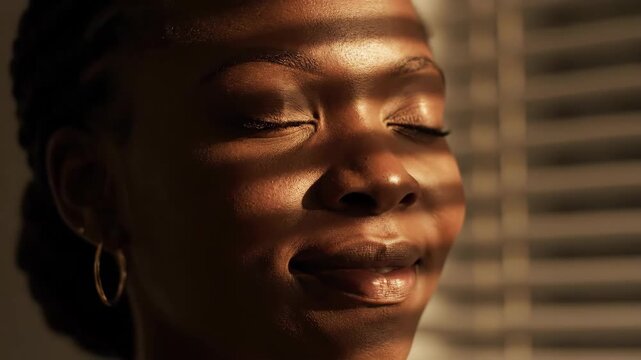 A close-up portrait of a person with closed eyes, illuminated by striped light. The warm light caresses the skin, highlighting the facial contours