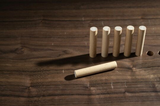 Five wooden dowels in a row with one lying beside drilled bench holes