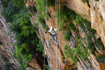 Climber Crossing High Rope Along Sandstone Canyon Cliff © TranThi